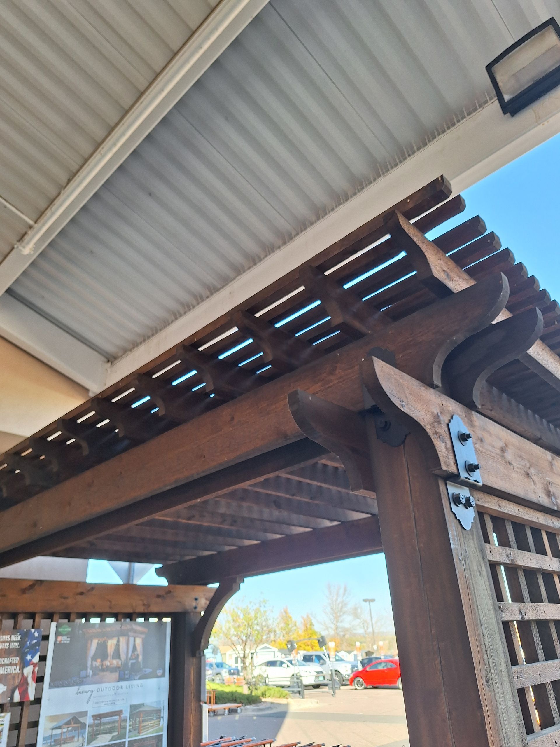 Wooden pergola with slatted roof and side lattice panels under a corrugated metal awning.