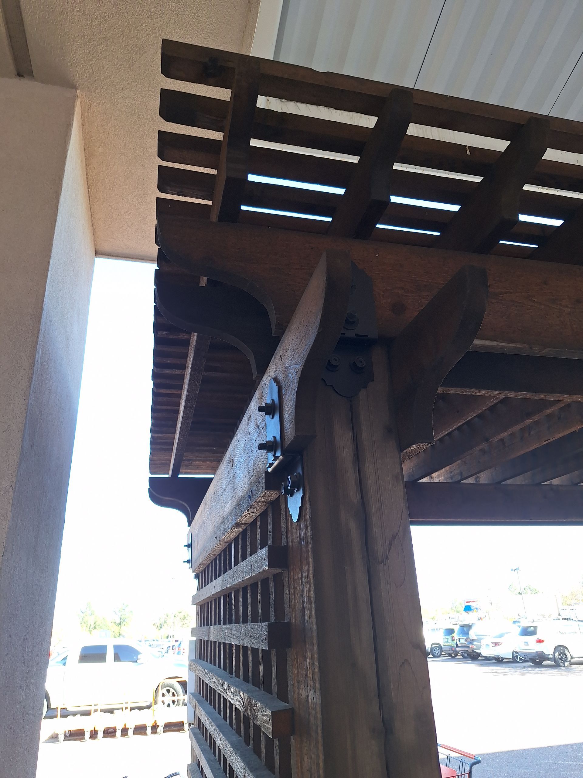 Wooden pergola post and beams with decorative brackets and lattice roof.
