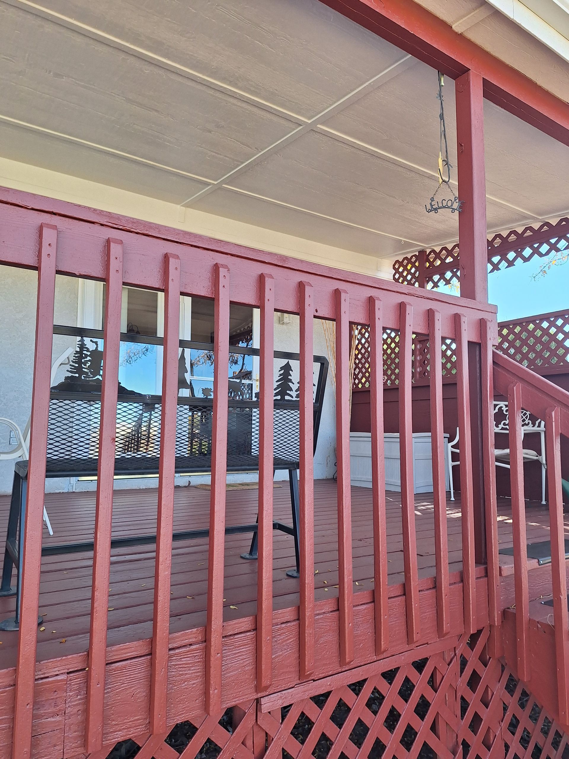 Red-painted porch with railing. Inside, a table and chairs. Overhang has decorative trim.