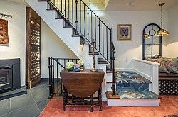 Staircase with black railing, table with flowers, small rug, and framed artwork.
