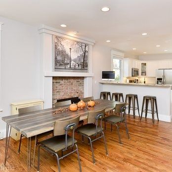 Dining room with wooden table, metal chairs, brick fireplace, and open kitchen.