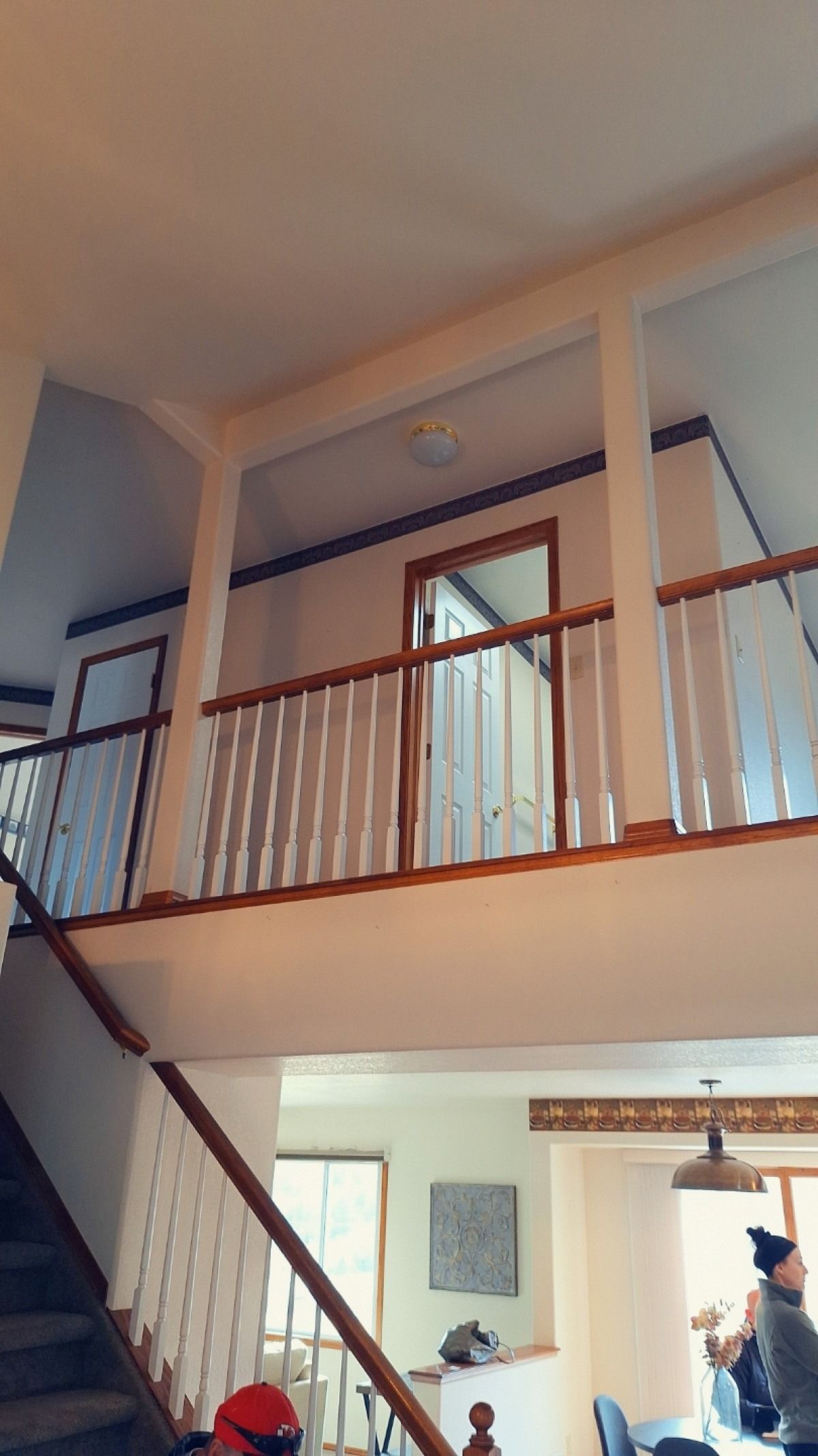 Two-story interior with staircase and balcony overlooking the lower level. White walls, wood railings, and brown trim.