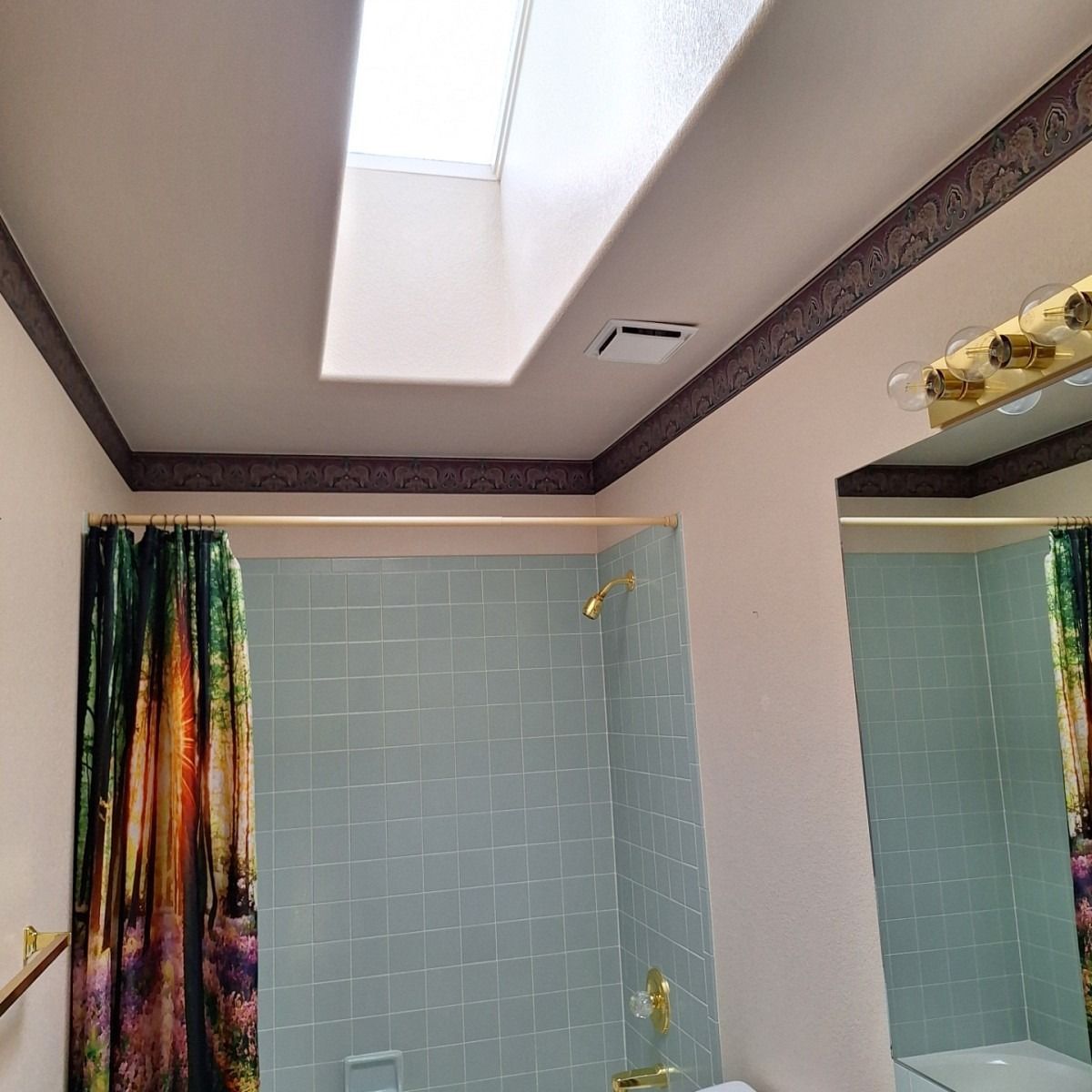 Bathroom with a skylight, shower, and mirror. Green shower tiles and a decorative border along the ceiling.