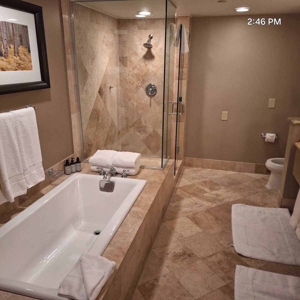 Bathroom with a tub, shower, and toilet; beige tile flooring and walls. White towels, neutral colors.