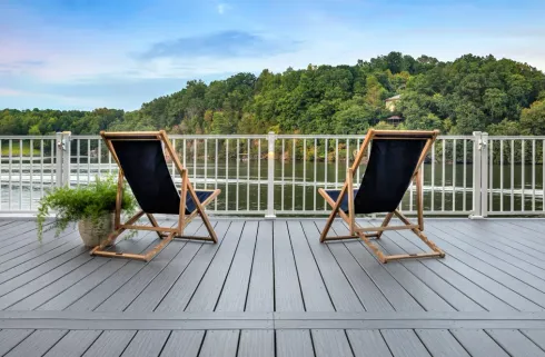Two lounge chairs on a deck overlooking a river, with a forest in the background.