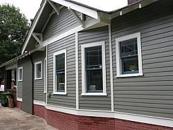 Gray house with white trim, brick base, and multiple windows.