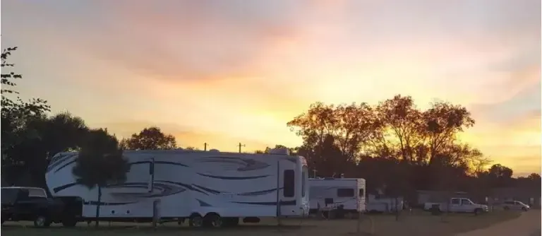 Campground scene with RVs silhouetted against a sunset sky with orange and pink hues.