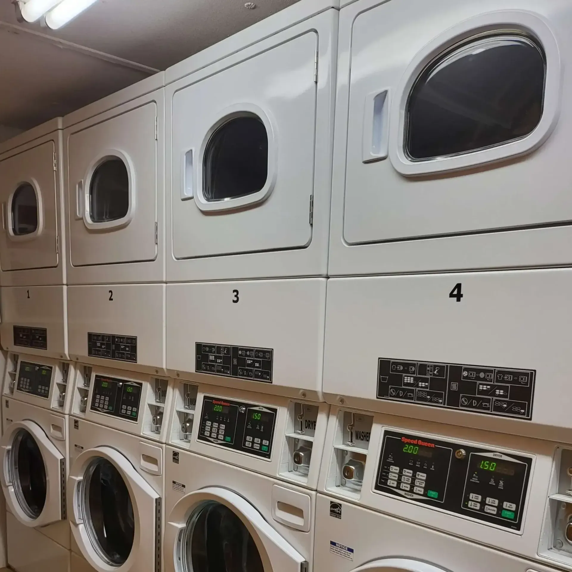 Row of washing machines and dryers in a laundromat. White appliances numbered 1-4.