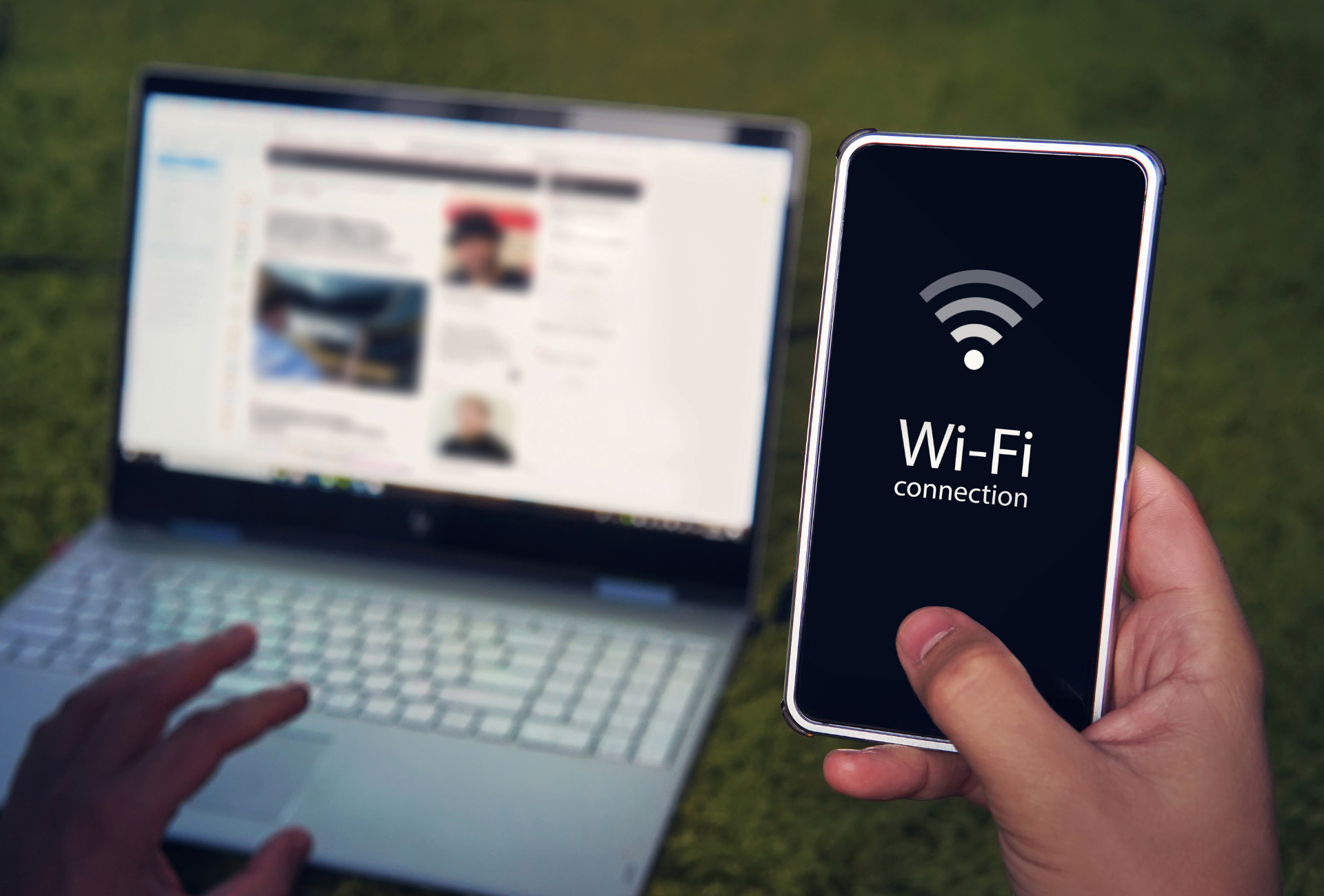 Person holding a phone displaying Wi-Fi signal; laptop open in background.