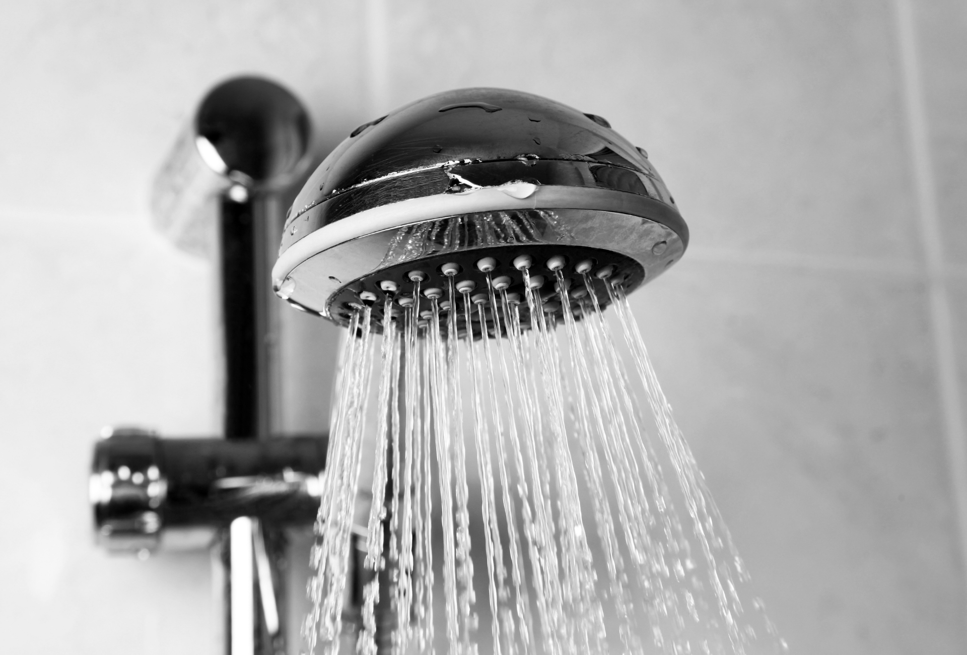 A chrome shower head with water spraying out. It is mounted on a wall with tiles.