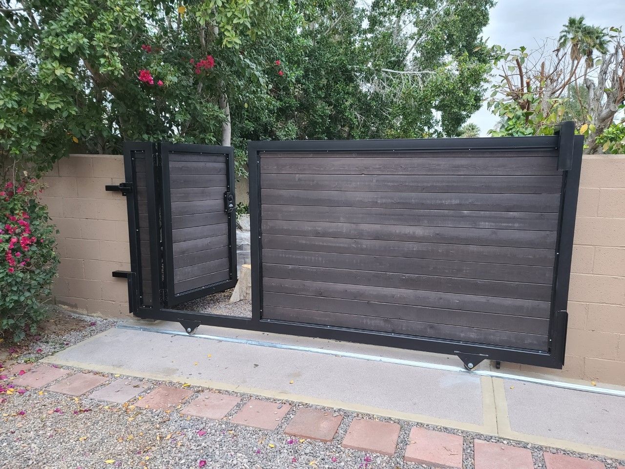 A black sliding gate with a wooden fence in the background.
