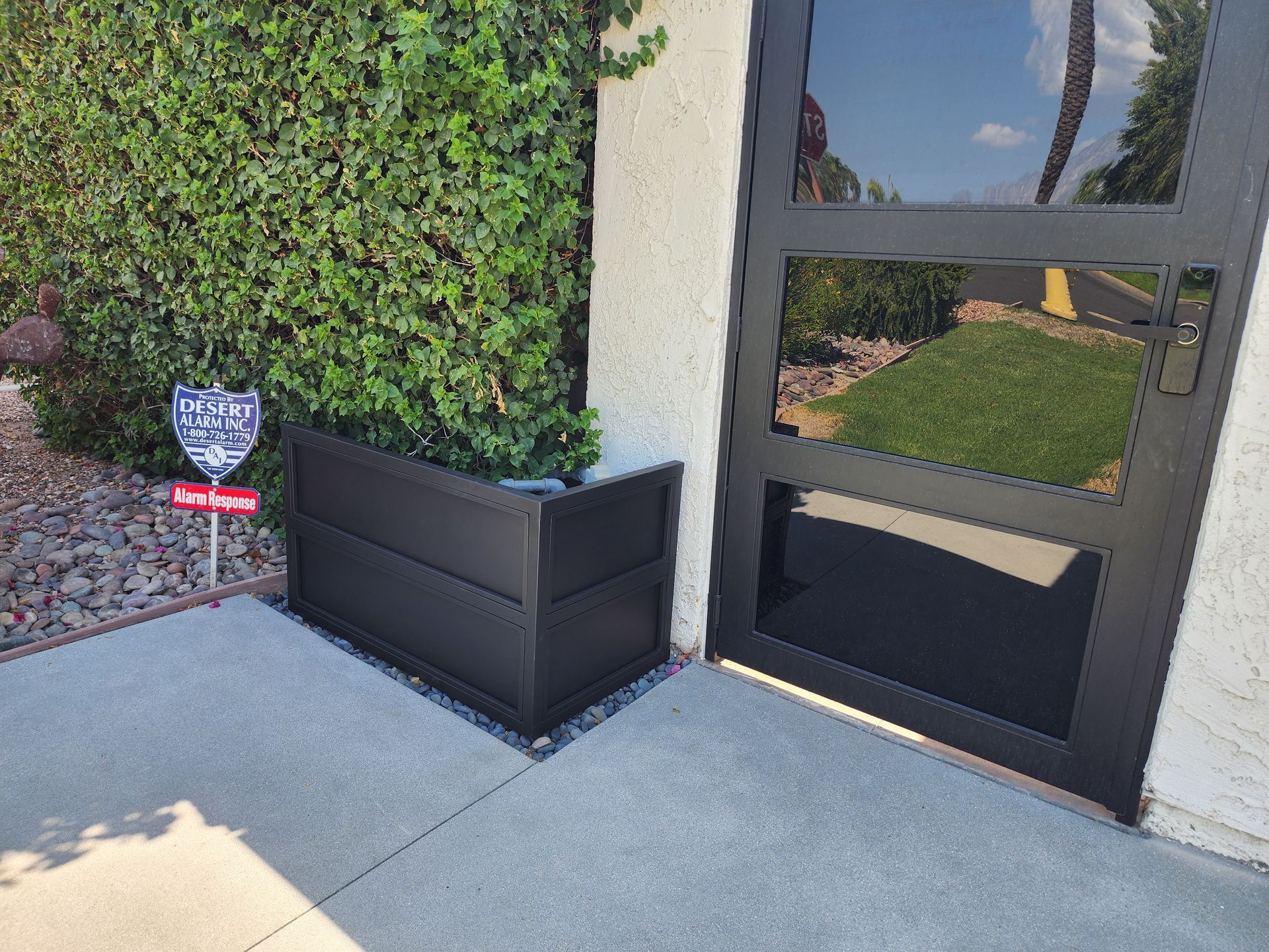 A black planter is sitting on the sidewalk next to a door.