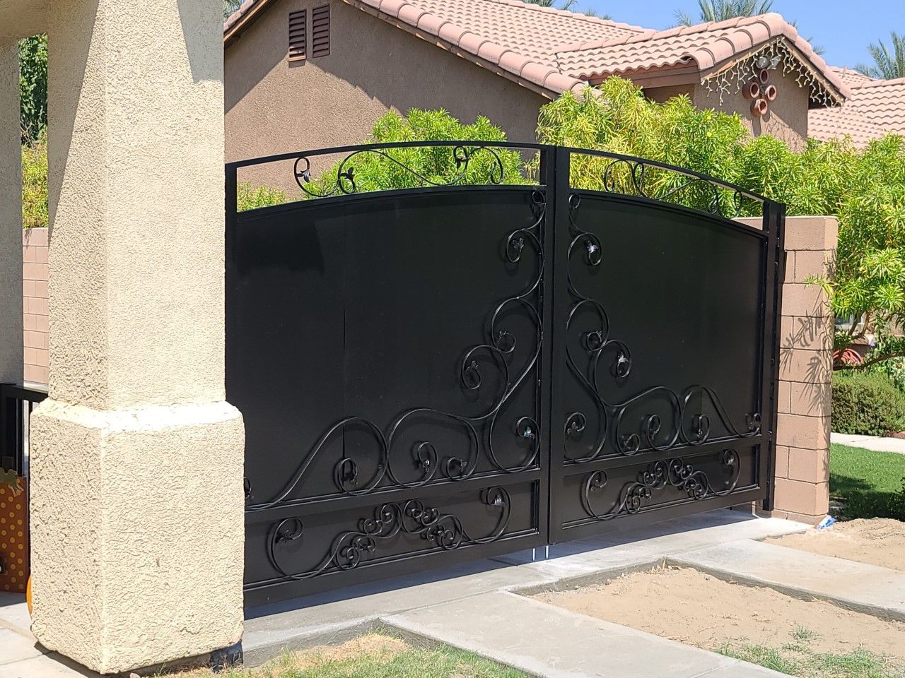 A black gate with a wrought iron design is in front of a house
