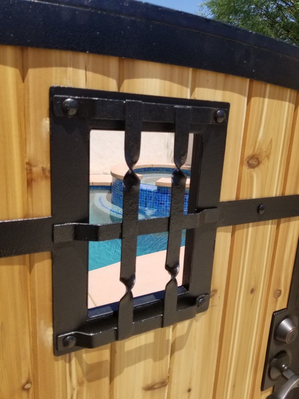 A wooden fence with a window that looks out to a pool