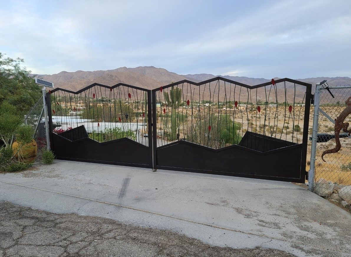 A black metal gate with mountains in the background is sitting on the side of a road.