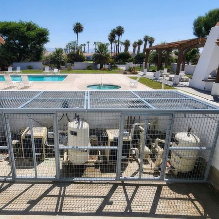 A fence surrounds a swimming pool with palm trees in the background