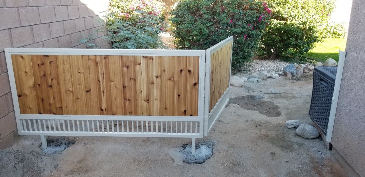 A wooden fence with a white railing is sitting in the dirt next to a brick wall.