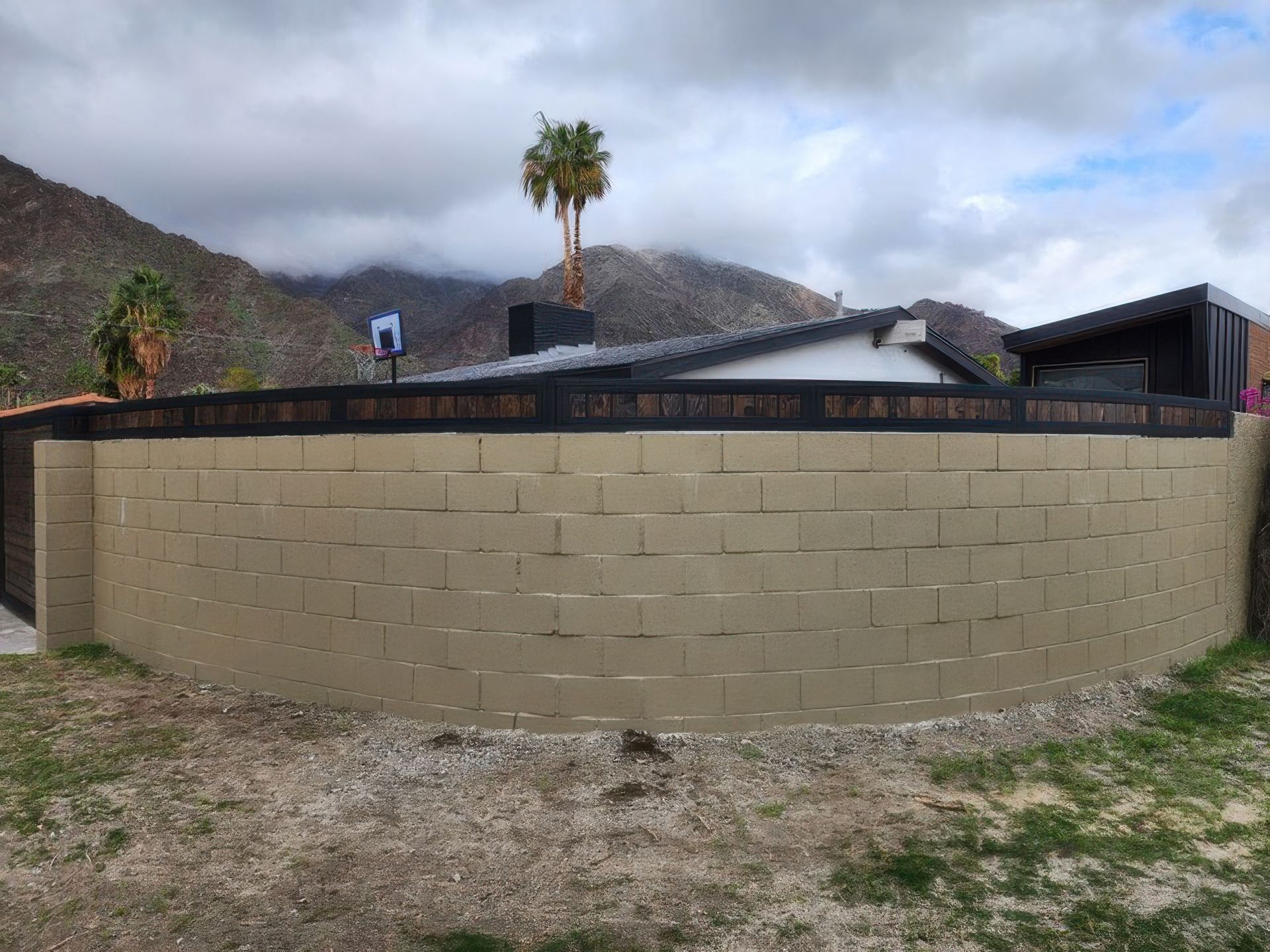 A large brick wall surrounds a house with mountains in the background.