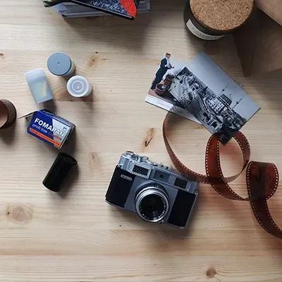Rolls of film, photo prints, 35mm negatives and camera on wooden table