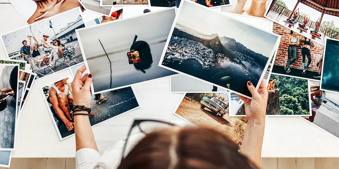 A woman holds multiple 8x10 bordered photo prints on a table, highlighting her cherished moments captured in high quality