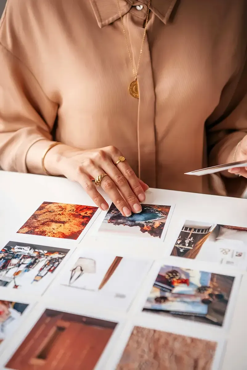 Square photo prints with white borders being organized on table.