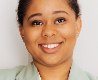 A woman in a green jacket is smiling for the camera.