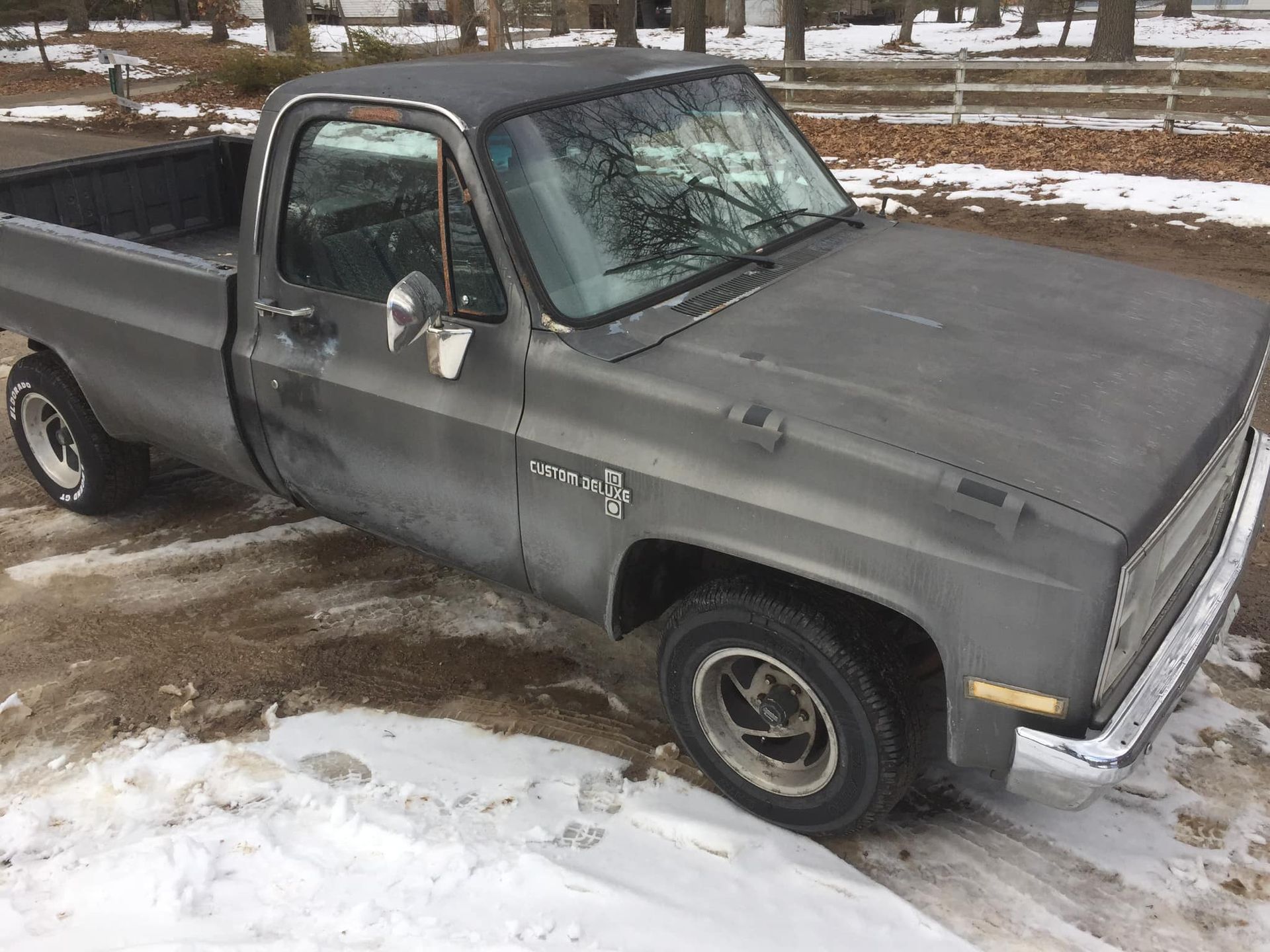 Grey Chevy pickup truck parked in the snow, featuring weathered paint and a black bed.