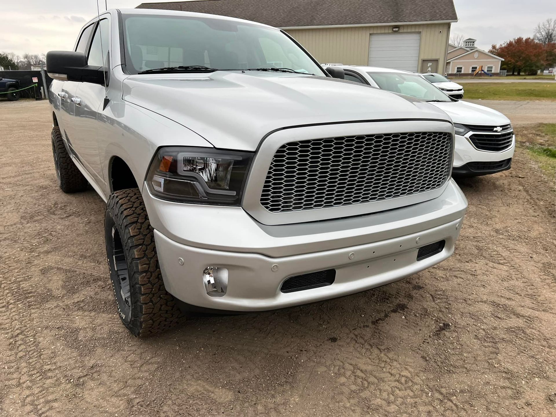 Silver Dodge Ram truck with black grill, parked outdoors on gravel.