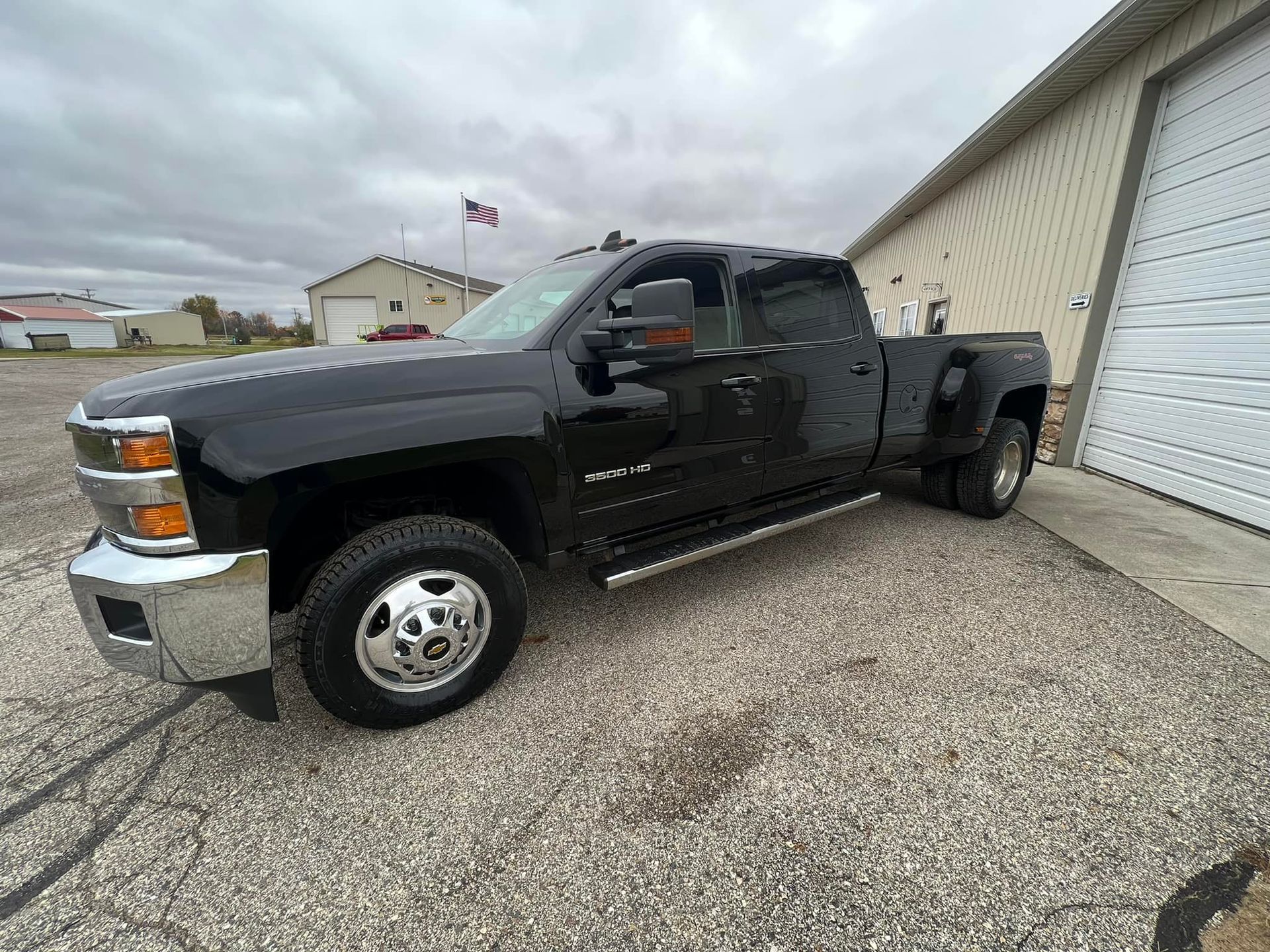 Black Chevy dually truck parked in front of a building on gravel under a cloudy sky.
