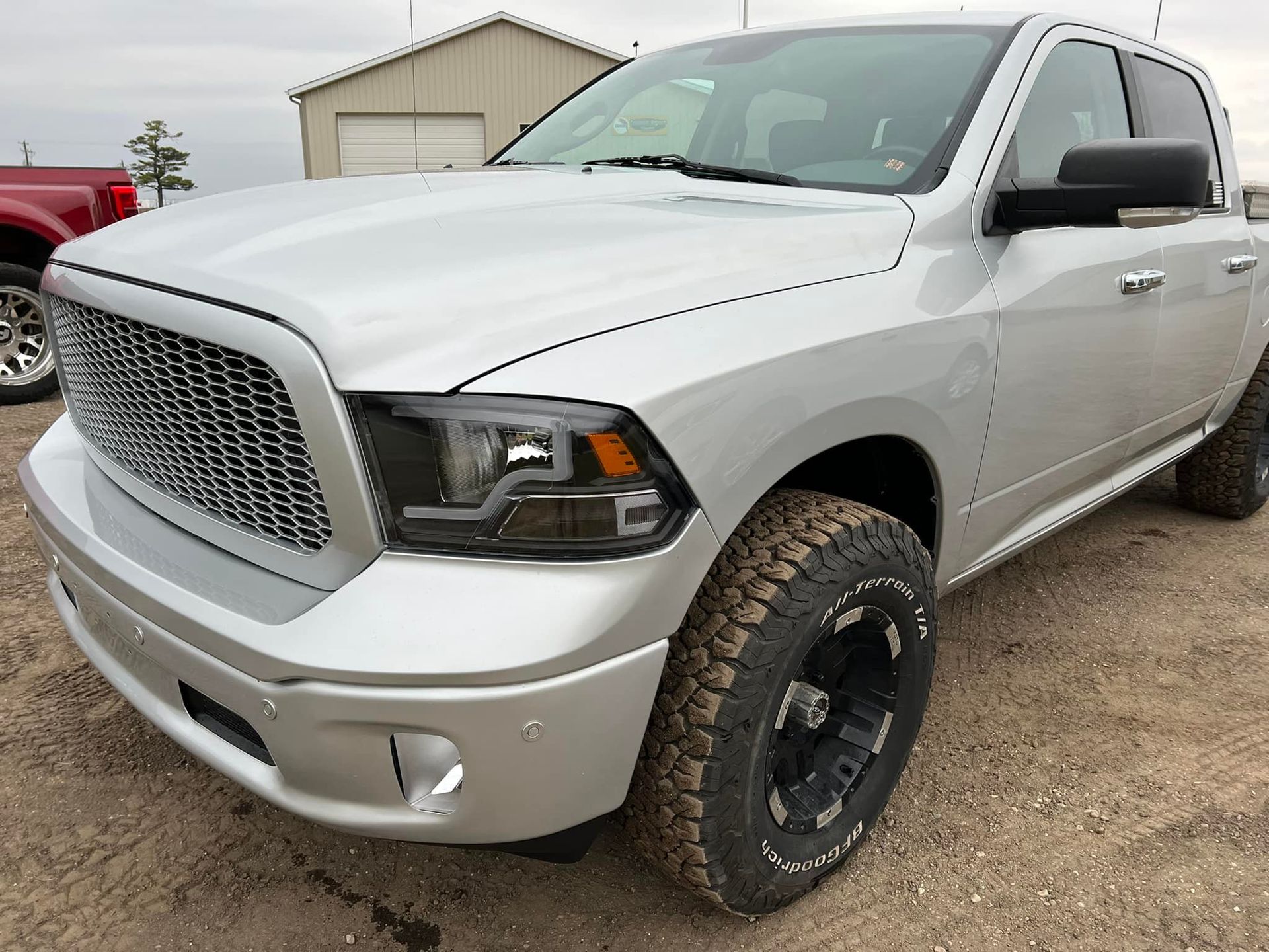 Silver Dodge Ram pickup truck with black wheels and grill, parked outdoors on a dirt lot.