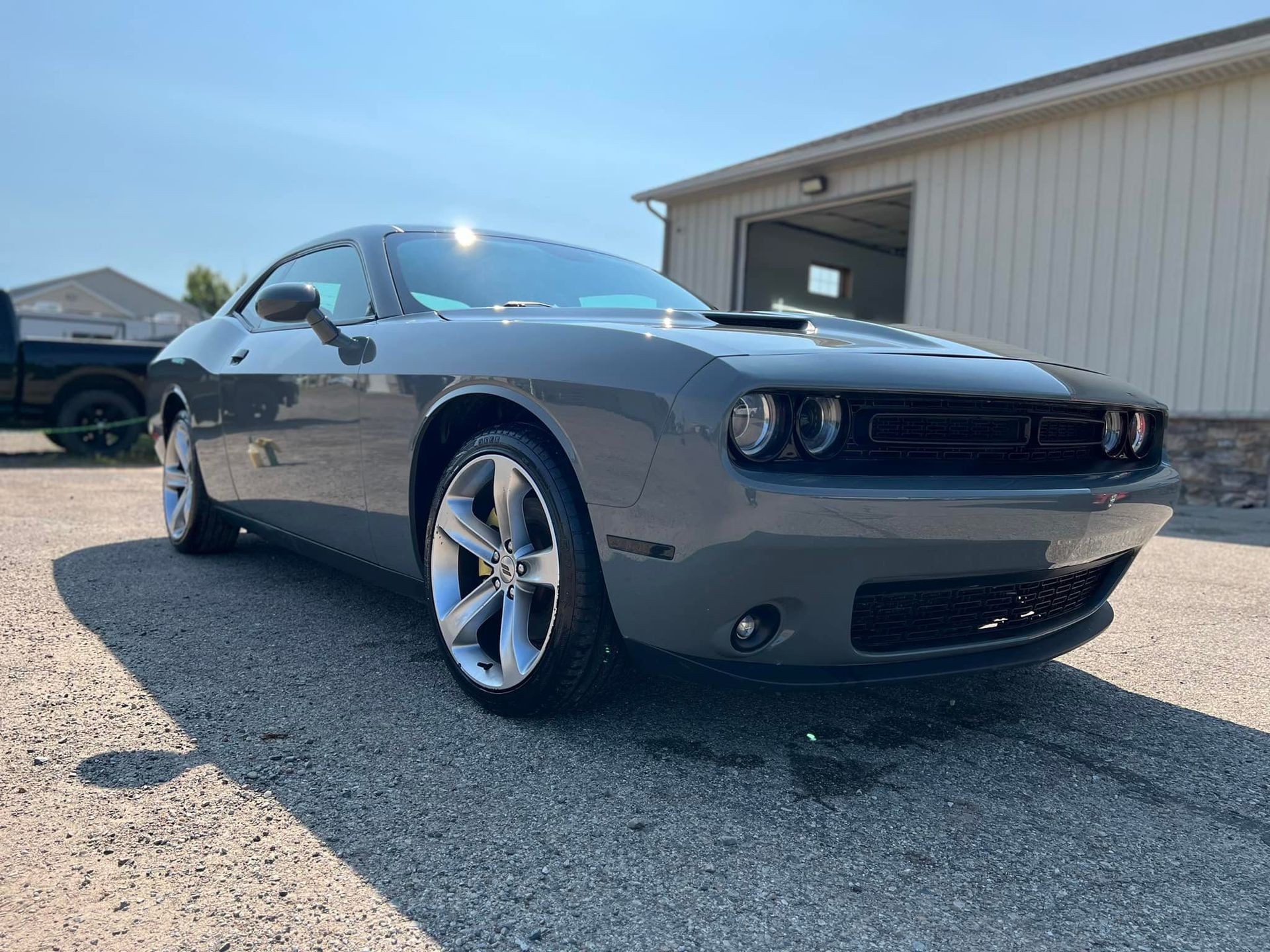 Gray Dodge Challenger parked on gravel, sunny day.