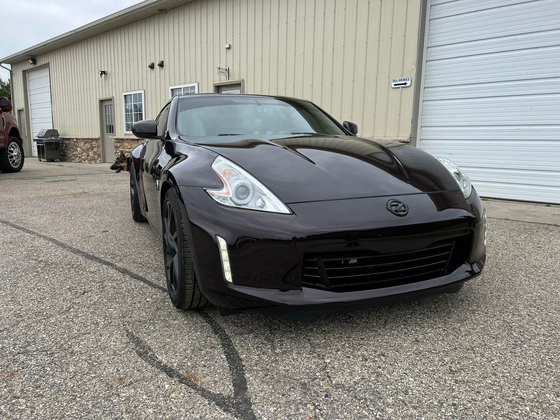 Dark burgundy Nissan 370Z sports car parked in front of a building with a white garage door.