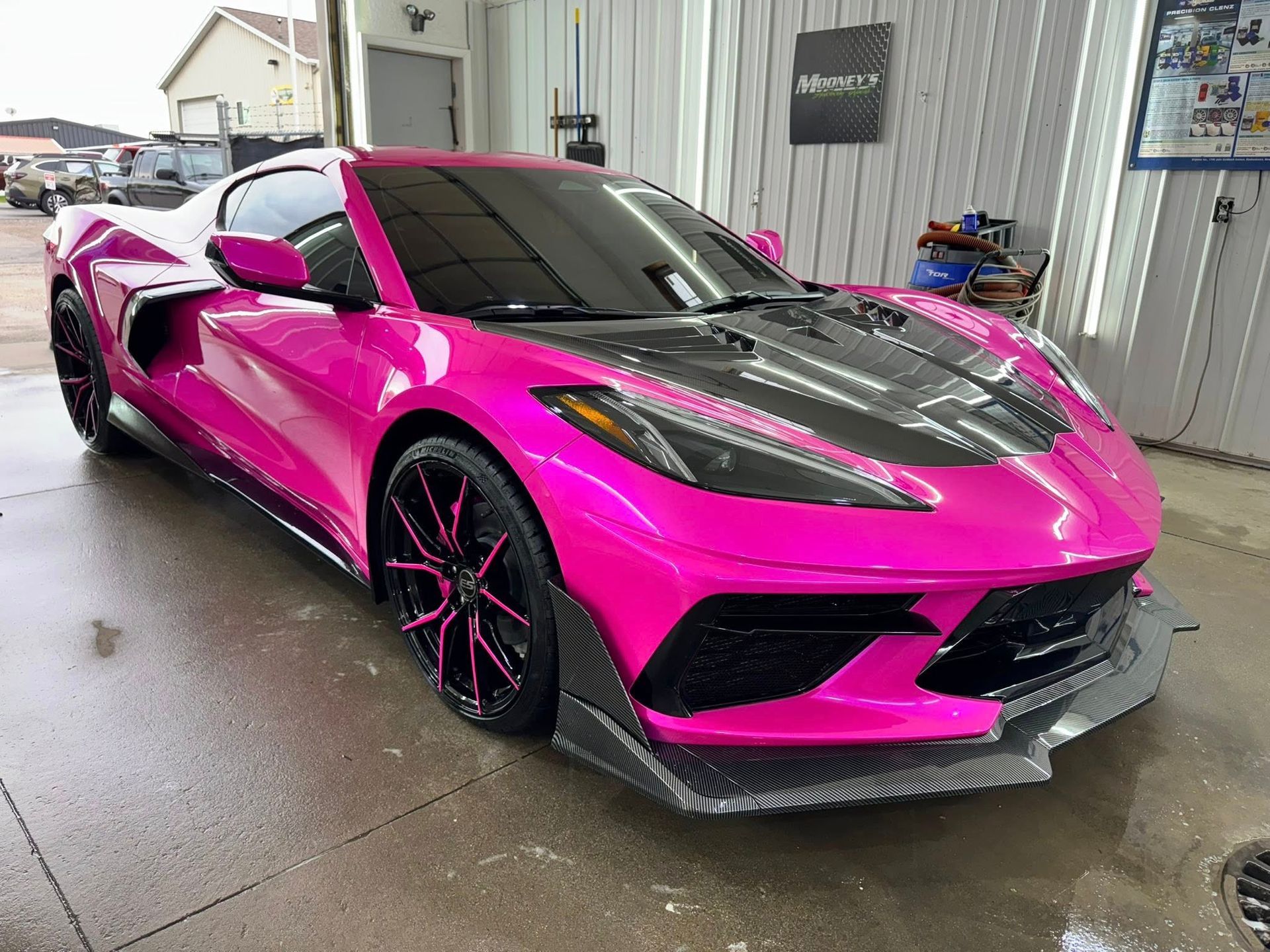 Pink Corvette sports car with black accents in a wash bay.