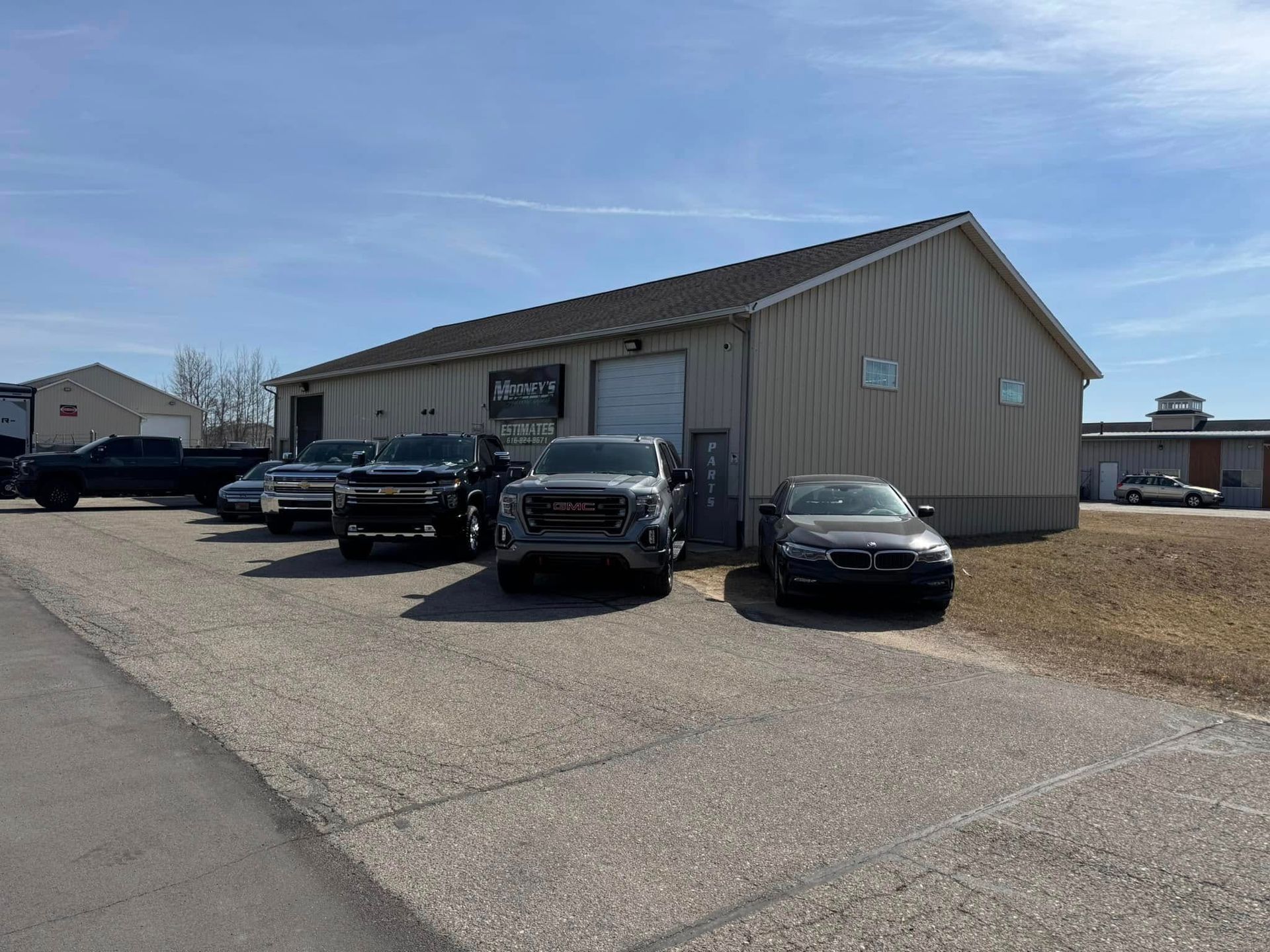 Vehicles parked in front of a tan building with a garage door, under a partly cloudy sky.