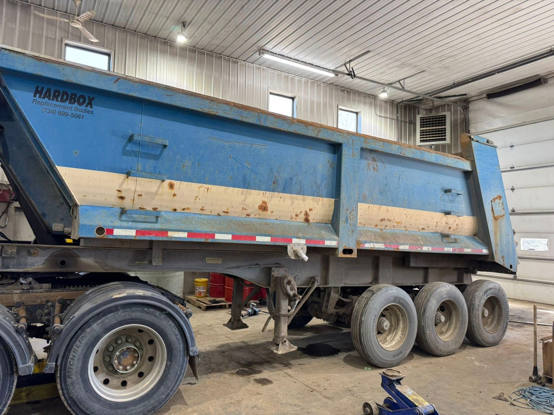 Blue dump truck trailer in a garage, showing rust and wear, under fluorescent lights.