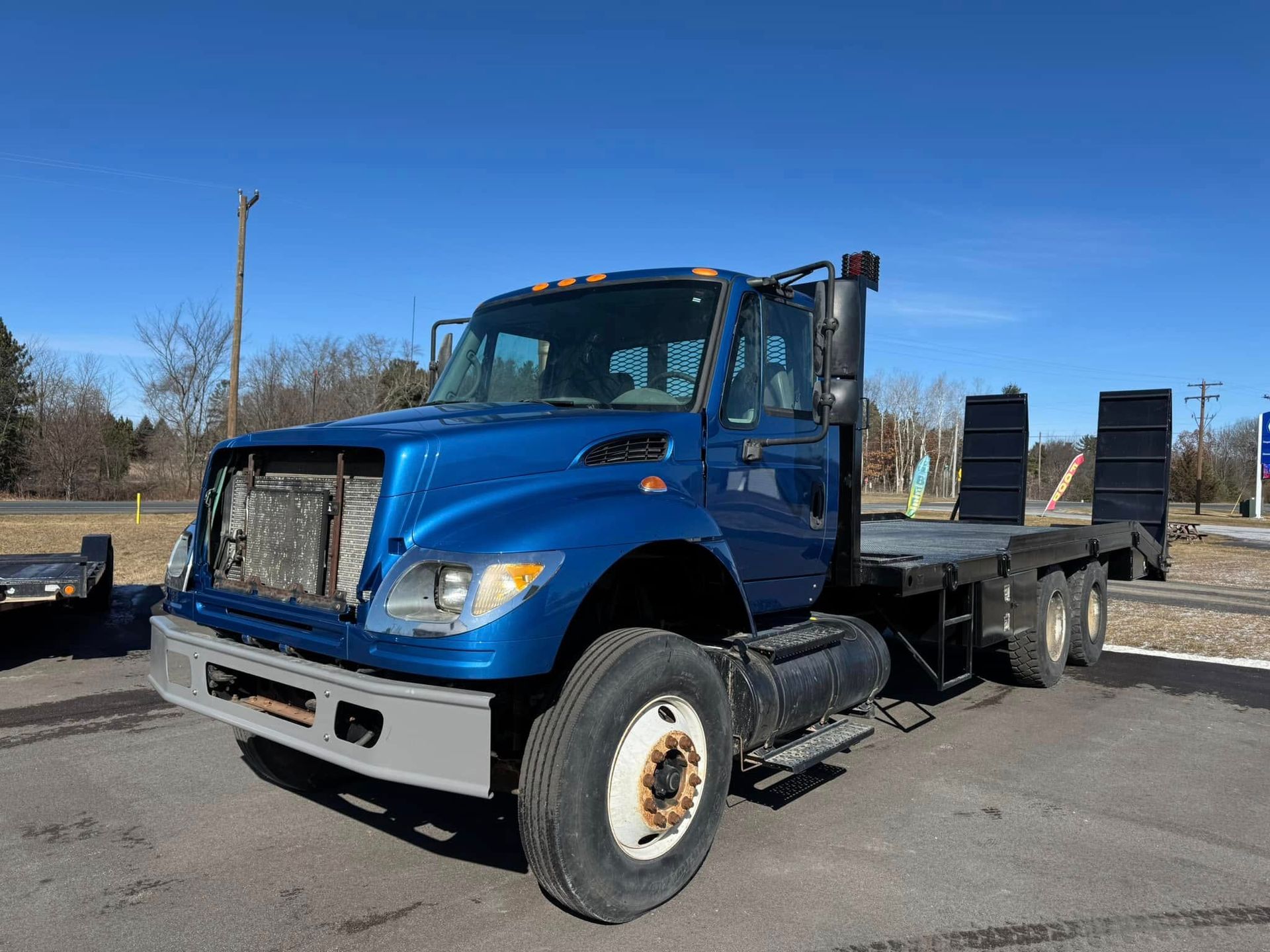 Blue International flatbed truck with missing grille parked outside on a sunny day.