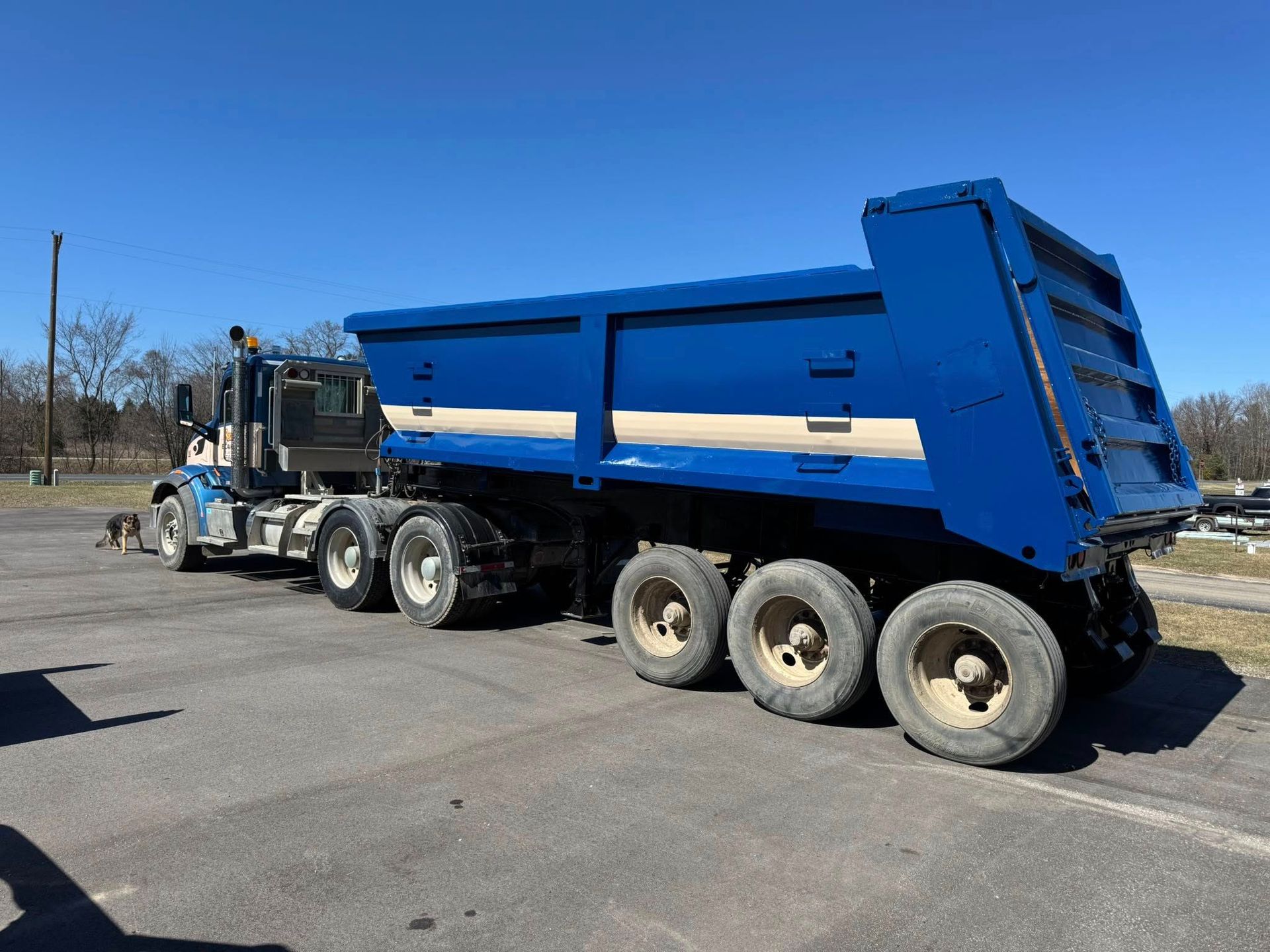 Blue dump truck parked on asphalt, against a clear sky.
