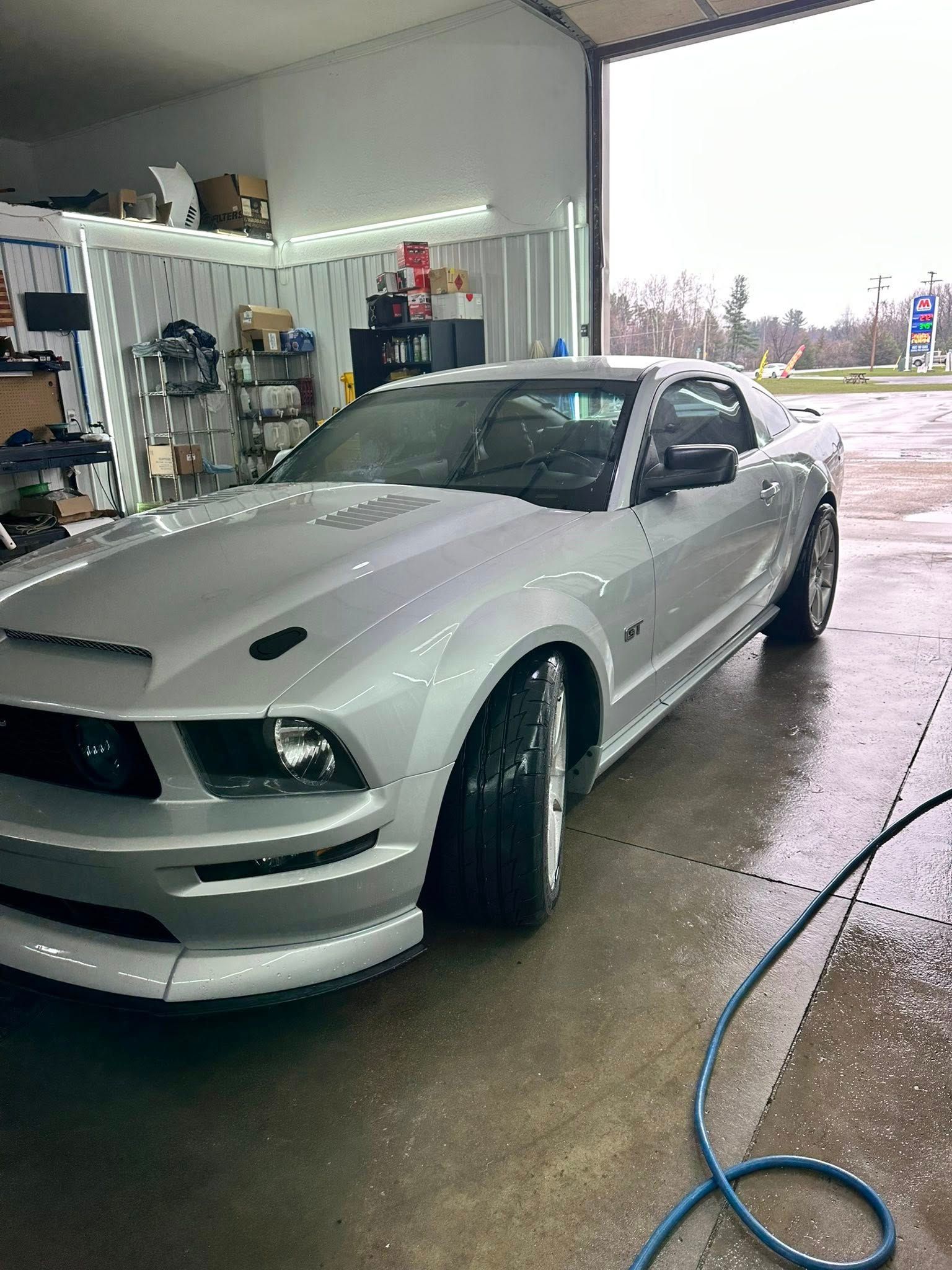 Silver Mustang sports car parked in a garage, with a hood scoop and wide tires.