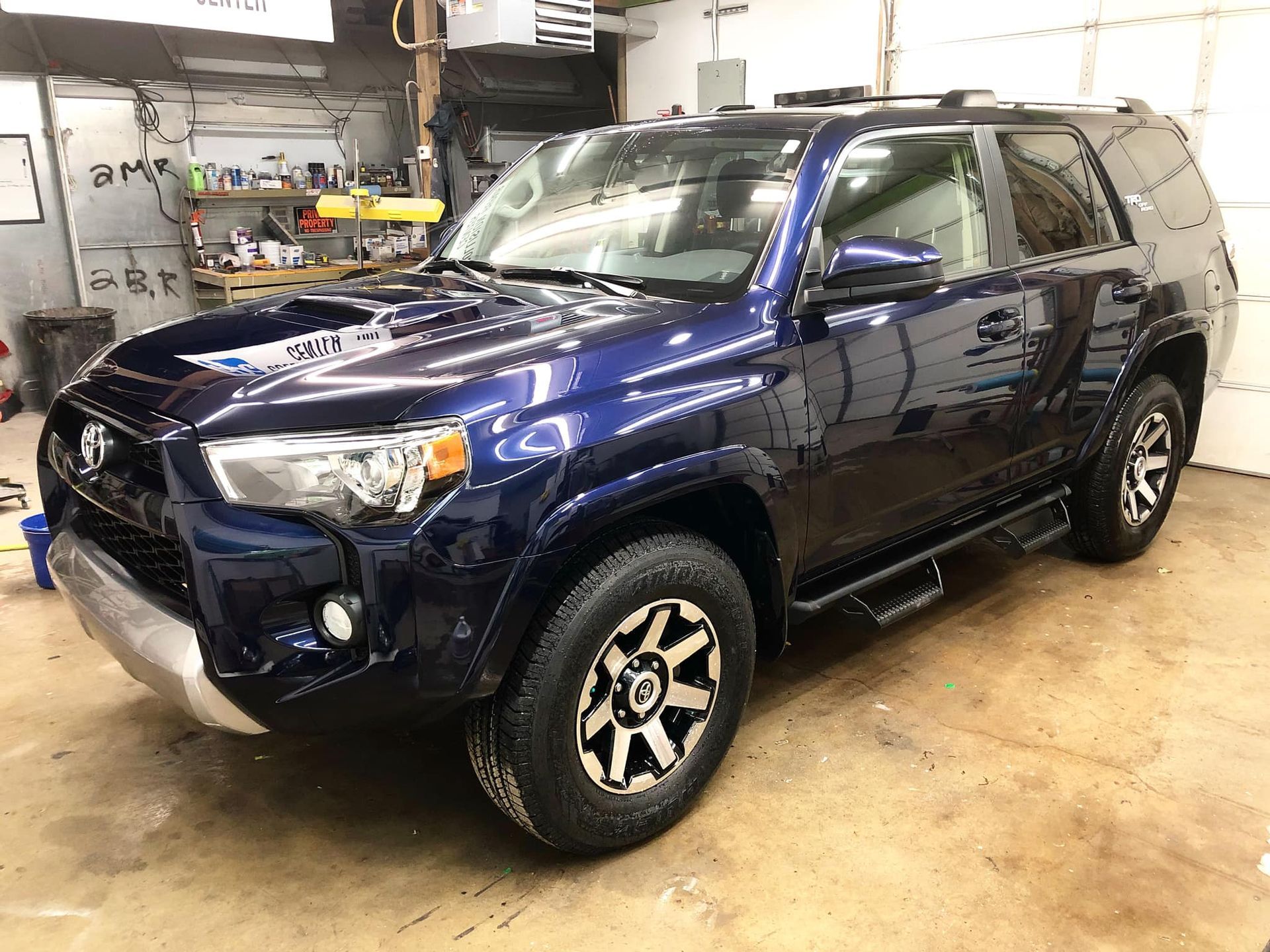 Dark blue Toyota 4Runner parked inside a garage. Silver accents, black wheels, and step bars visible.