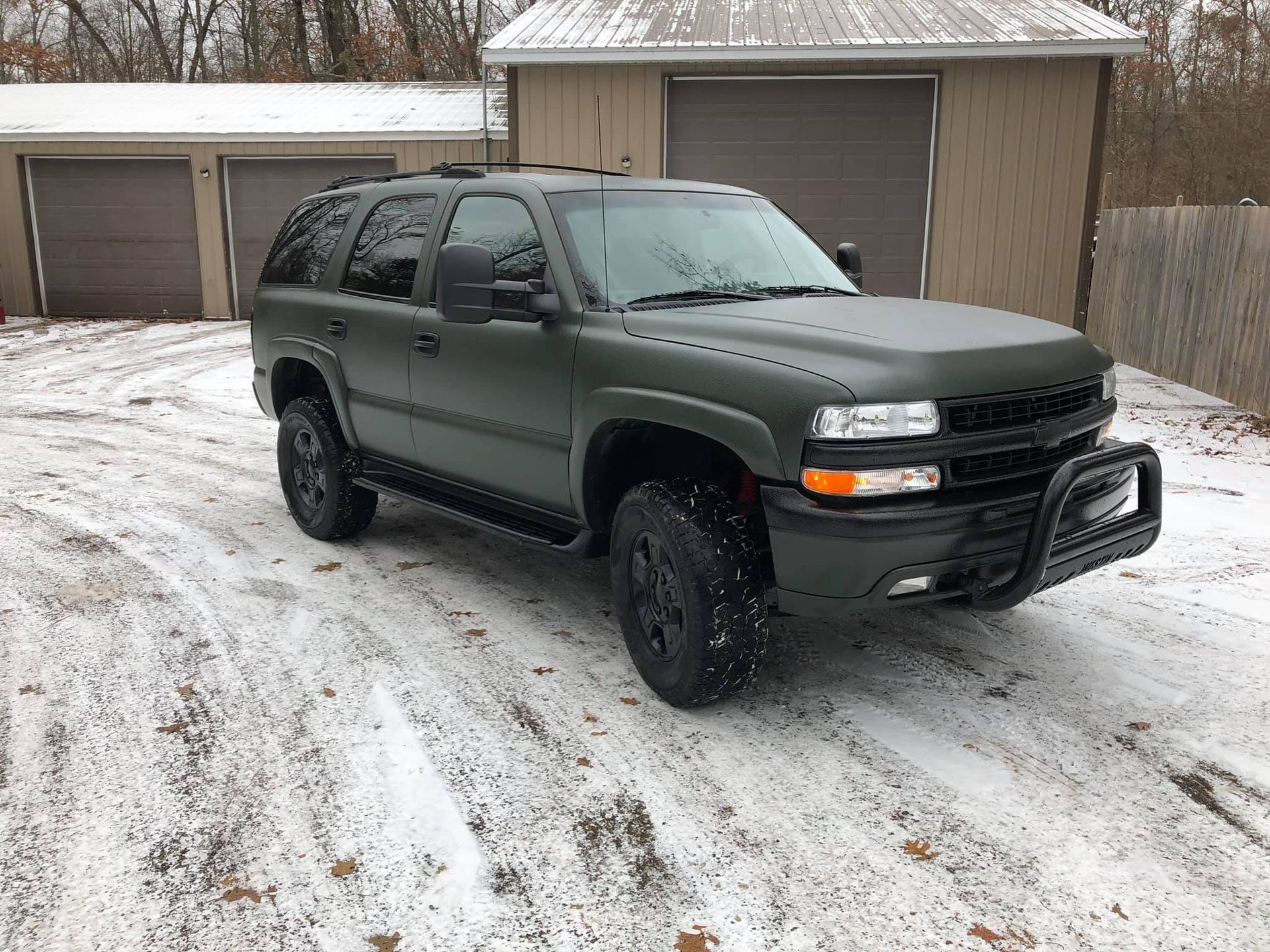 Green SUV parked in snow, with a black brush guard and wheels, in front of a garage.