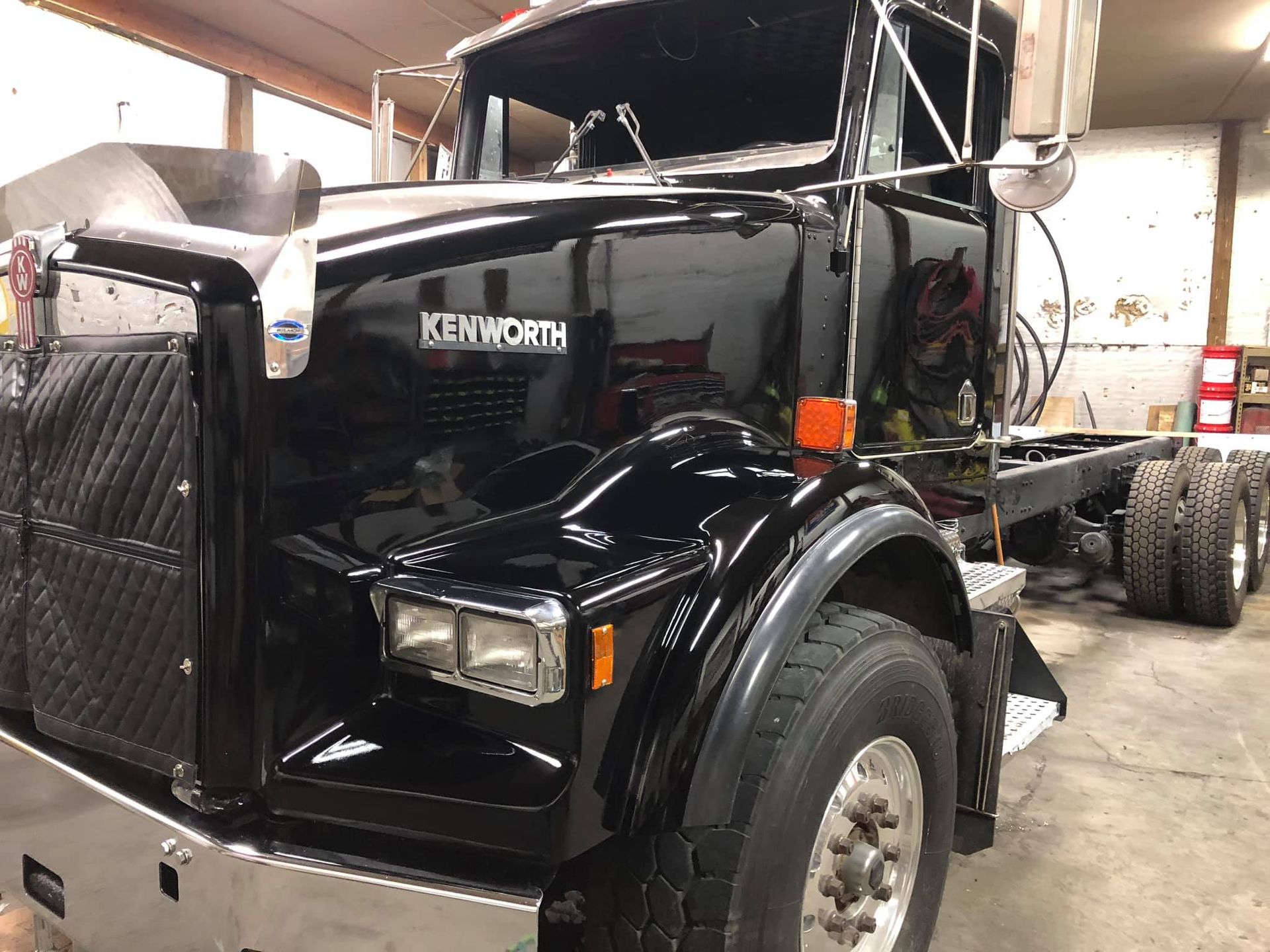 Black Kenworth truck, parked inside a garage; shiny black paint, chrome accents.