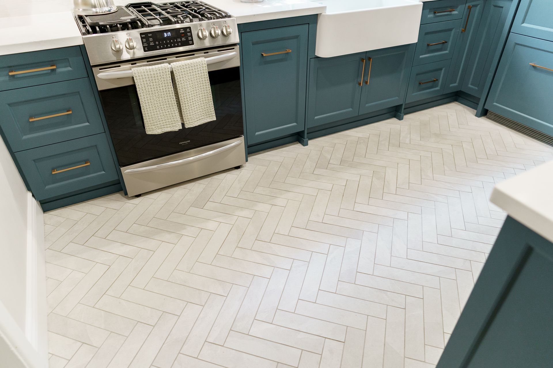 Teal kitchen cabinets, stainless stove, and white herringbone tile floor.