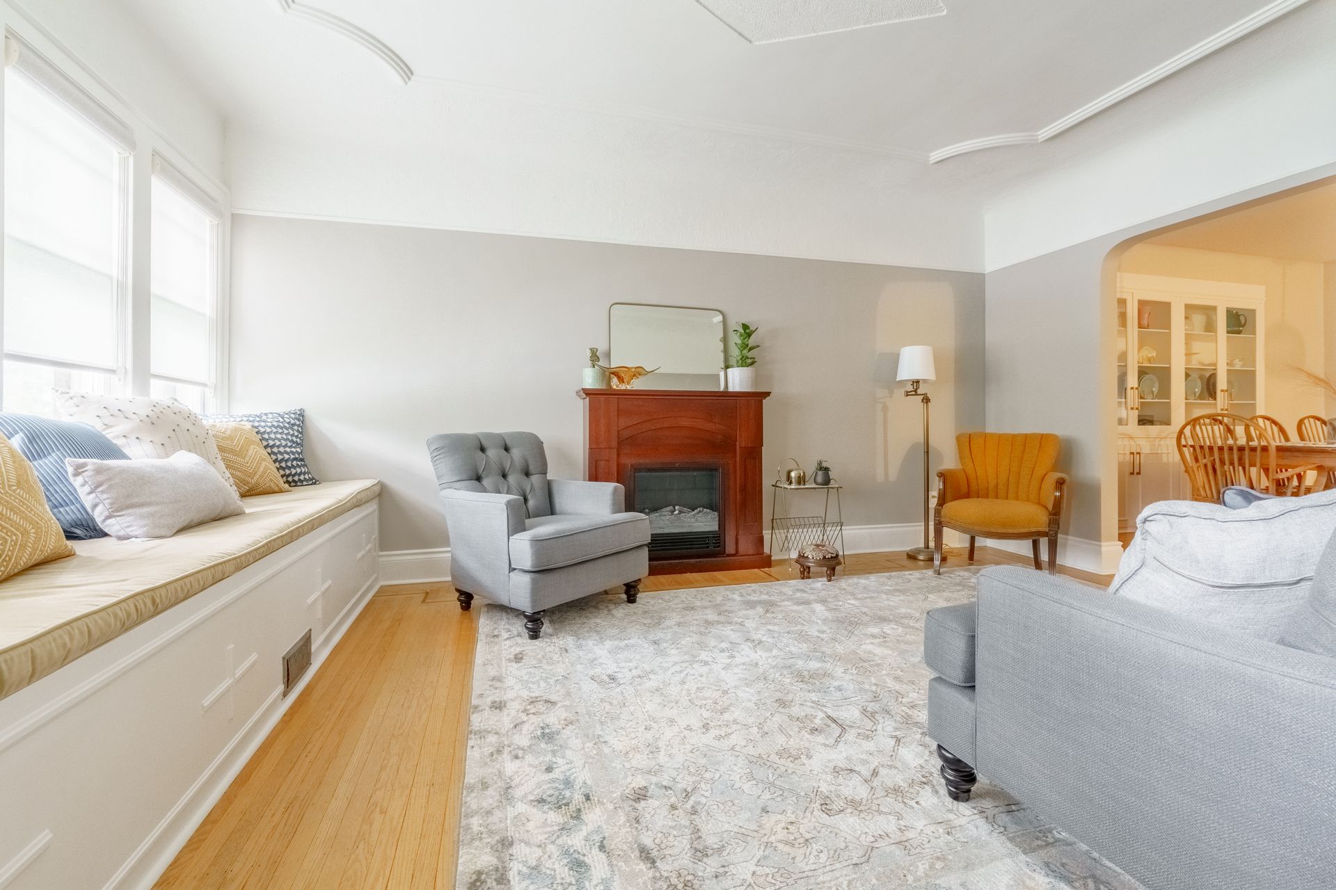 Bright living room with gray chairs, a white daybed, wood floors, and a red fireplace mantle