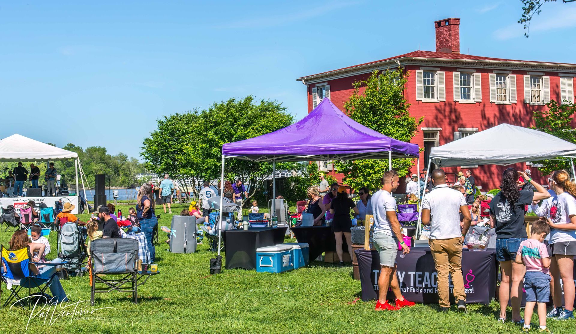 Outdoor event with vendors and a crowd in front of a red building under a sunny sky.