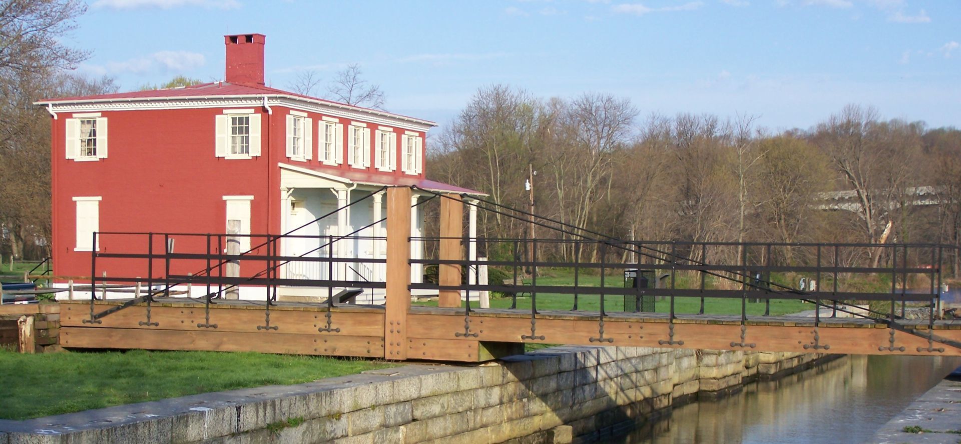 Red house with white trim by a canal; a wooden bridge spans the water.