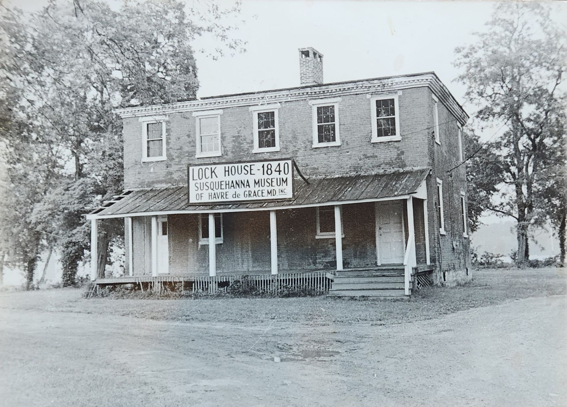 Two-story Lock House Museum, brick building with porch, trees surround, gray scale.