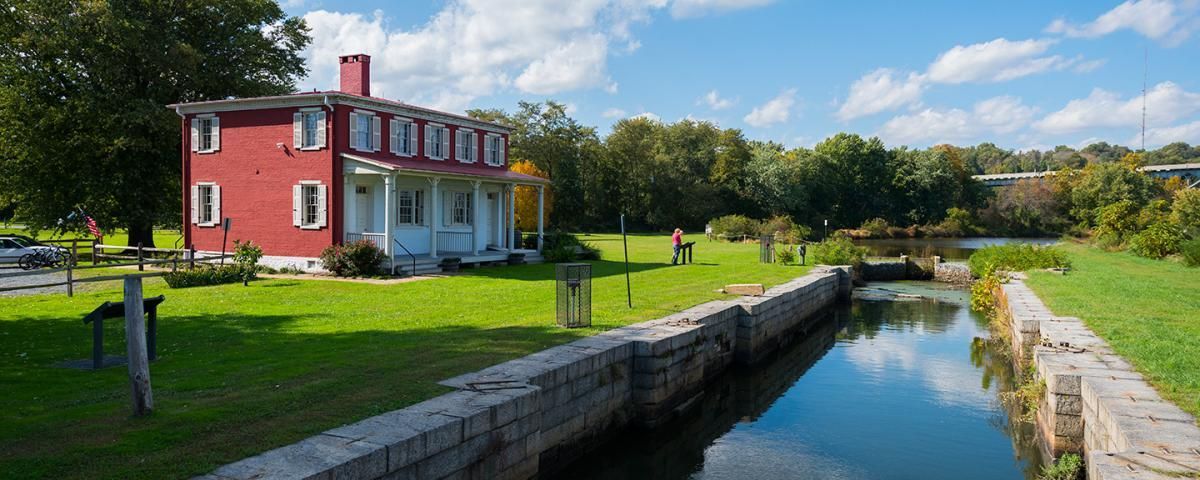 Red house on a canal with blue water, green grass, and a bright sky.