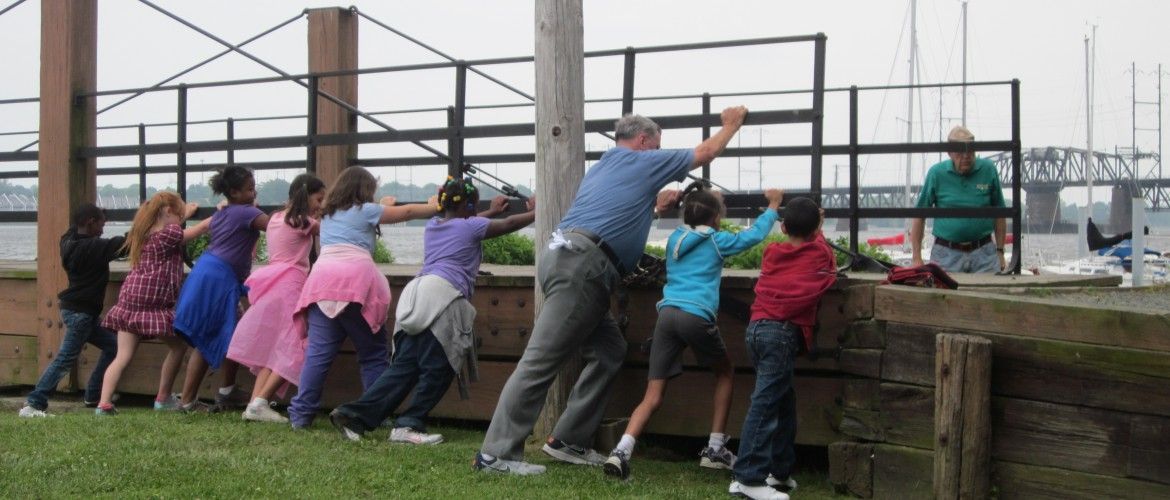 Children and a man pushing against a wooden barrier on the waterfront.