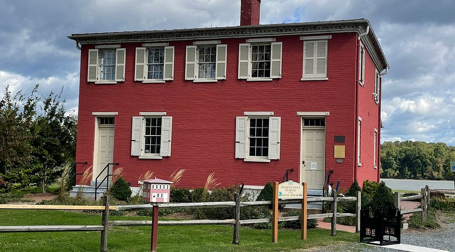 Red brick two-story house with white shutters. Wooden fence and mailbox in front, cloudy sky.