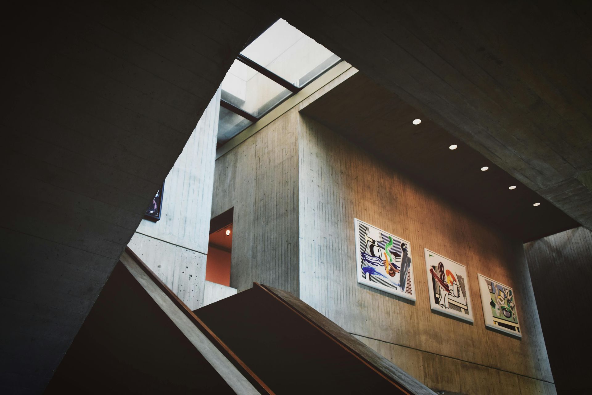 Concrete interior with a staircase, art on the wall, and natural light from above.